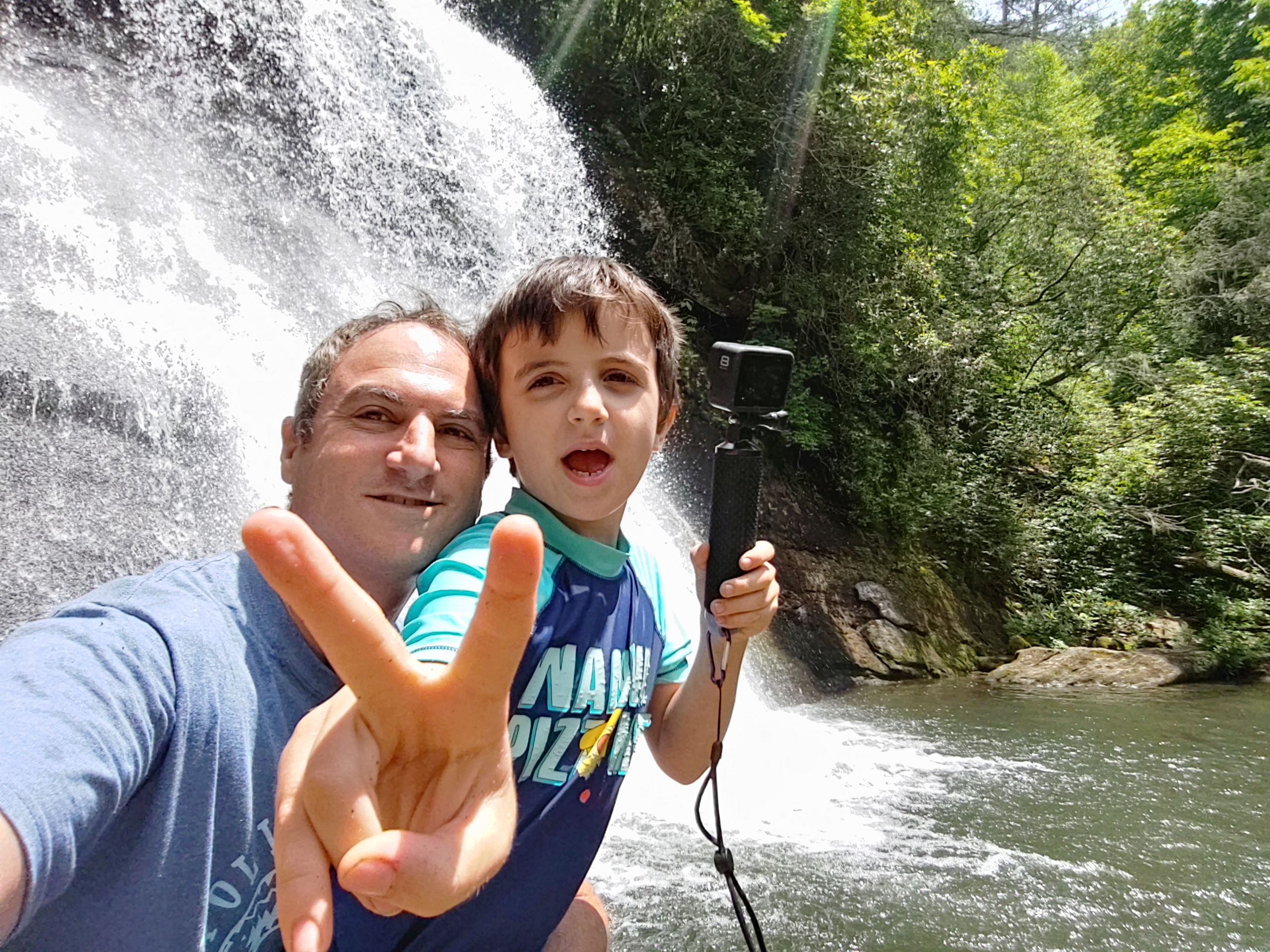 Father and young son taking a selfie with the towering 120-foot Mingo Falls in the background near Cherokee NC