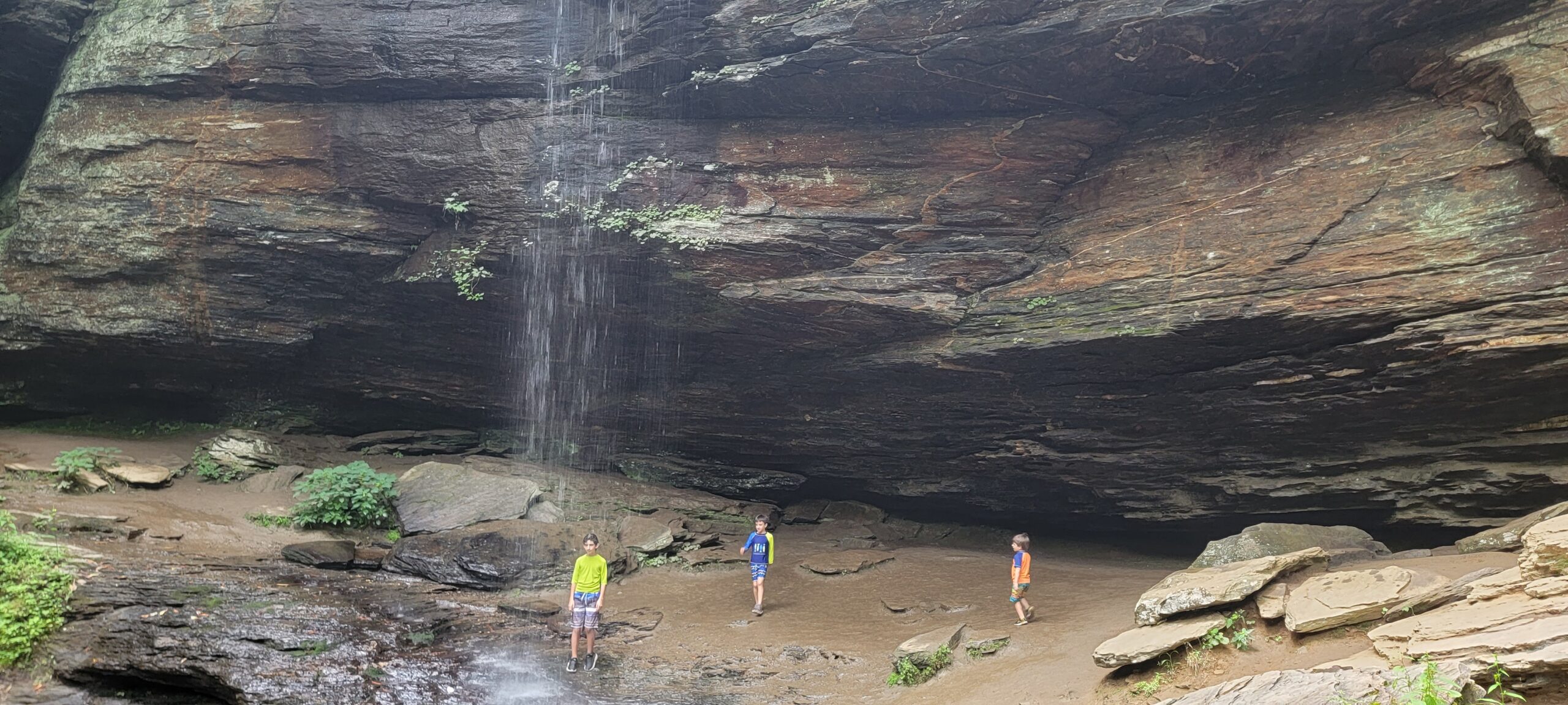 Two children standing behind the curtain of Moore Cove Falls, a 50-foot waterfall in Pisgah National Forest near Brevard NC