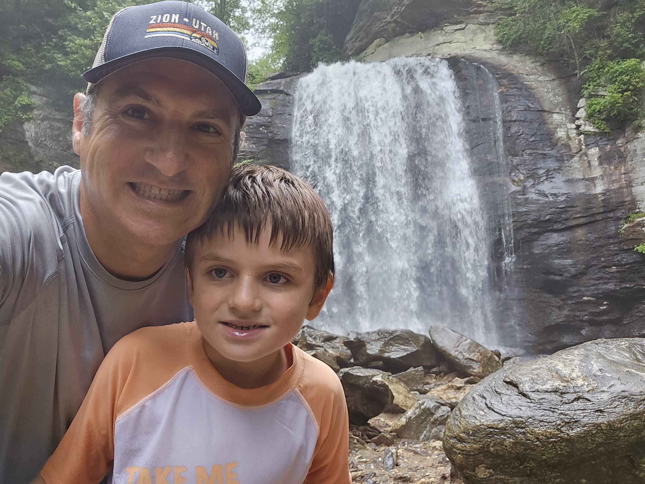 Father and son posing at the base of Looking Glass Falls, a wide 60-foot cascade in Pisgah National Forest NC