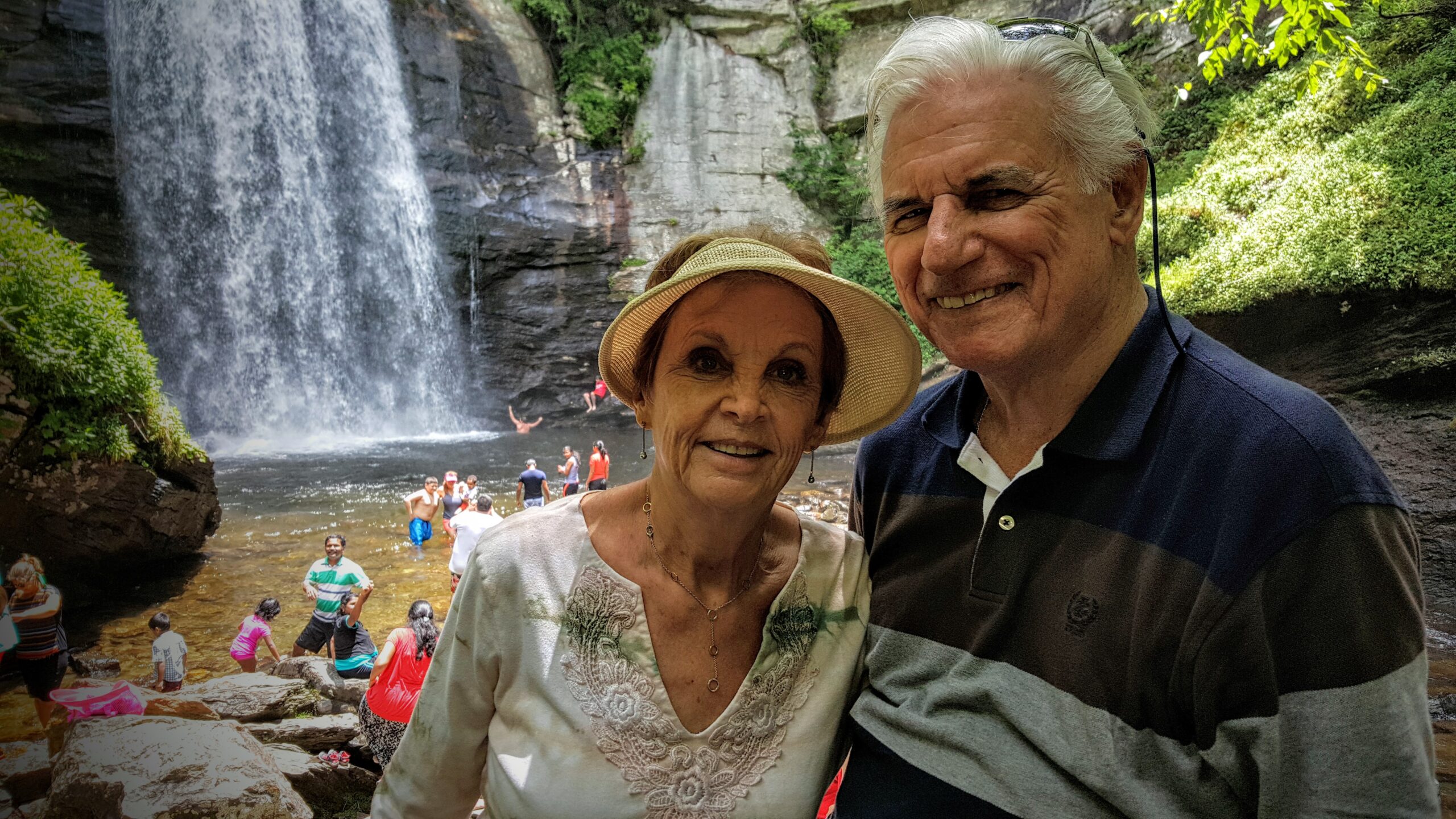 Couple standing at the Looking Glass Falls overlook with the 60-foot waterfall behind them in a lush green forest setting