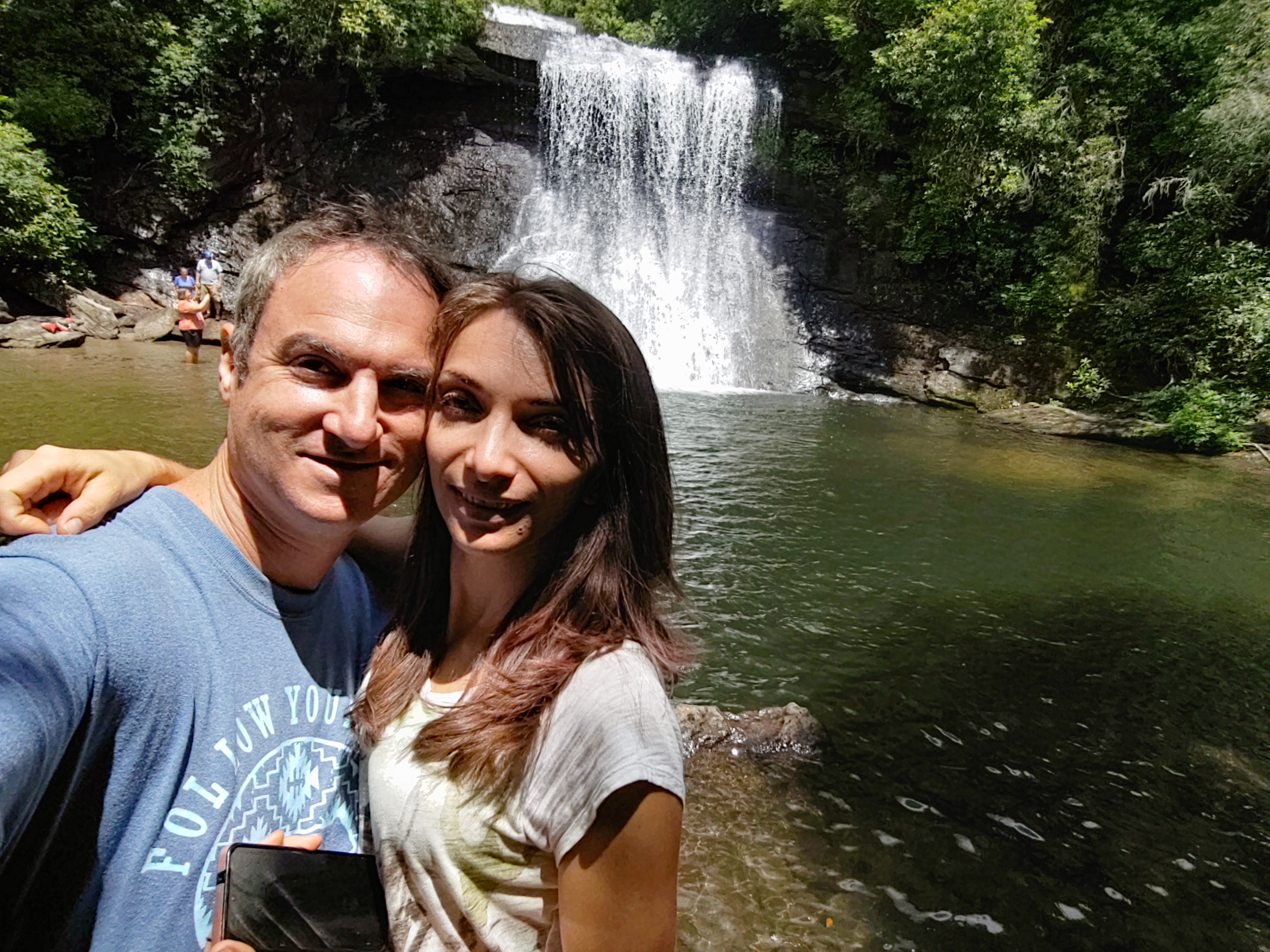 Couple taking a selfie at Hooker Falls in DuPont State Forest with the broad waterfall cascading behind them