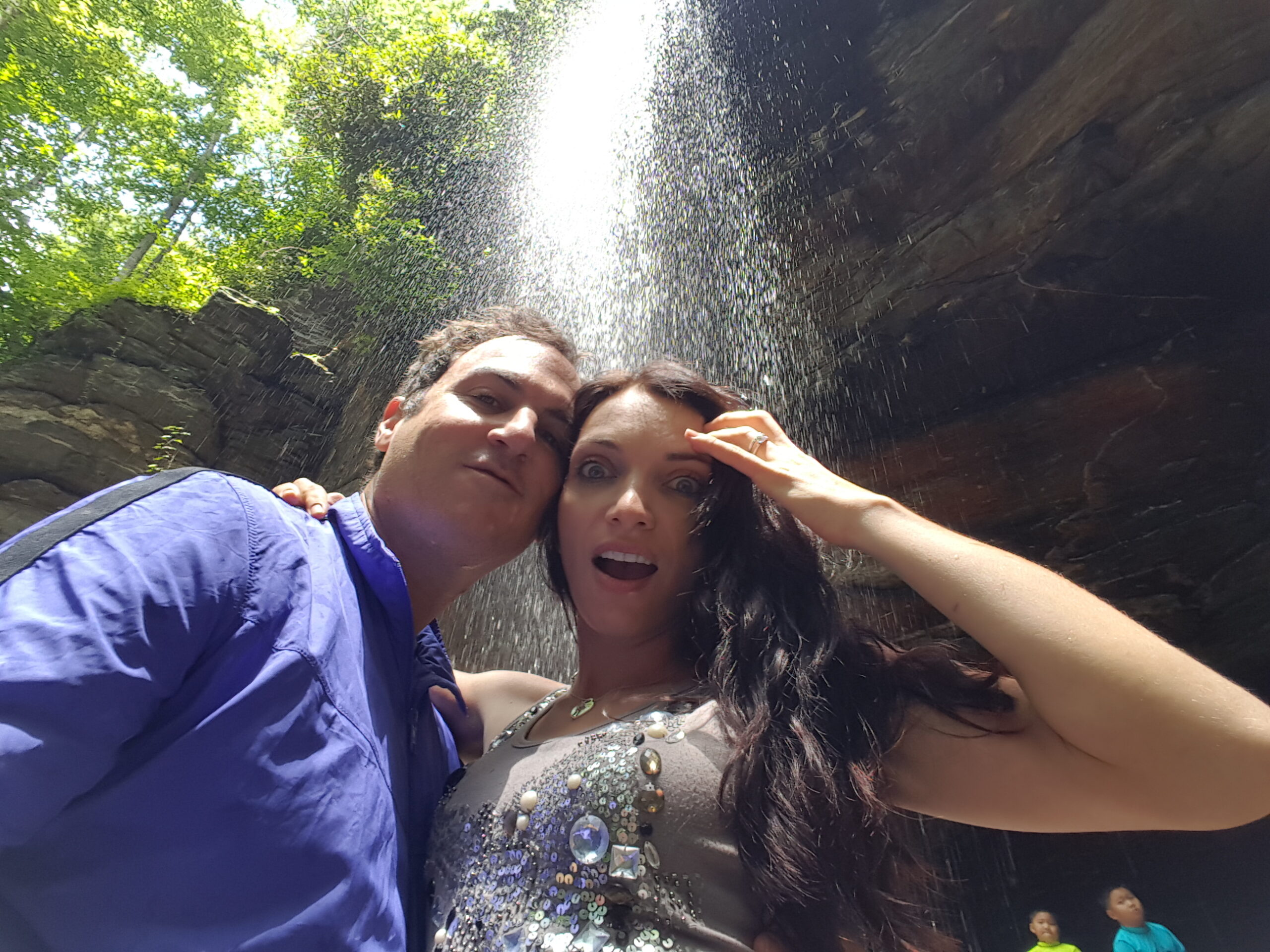 Person taking a selfie behind the 75-foot curtain of water at Dry Falls near Highlands NC with misty spray all around