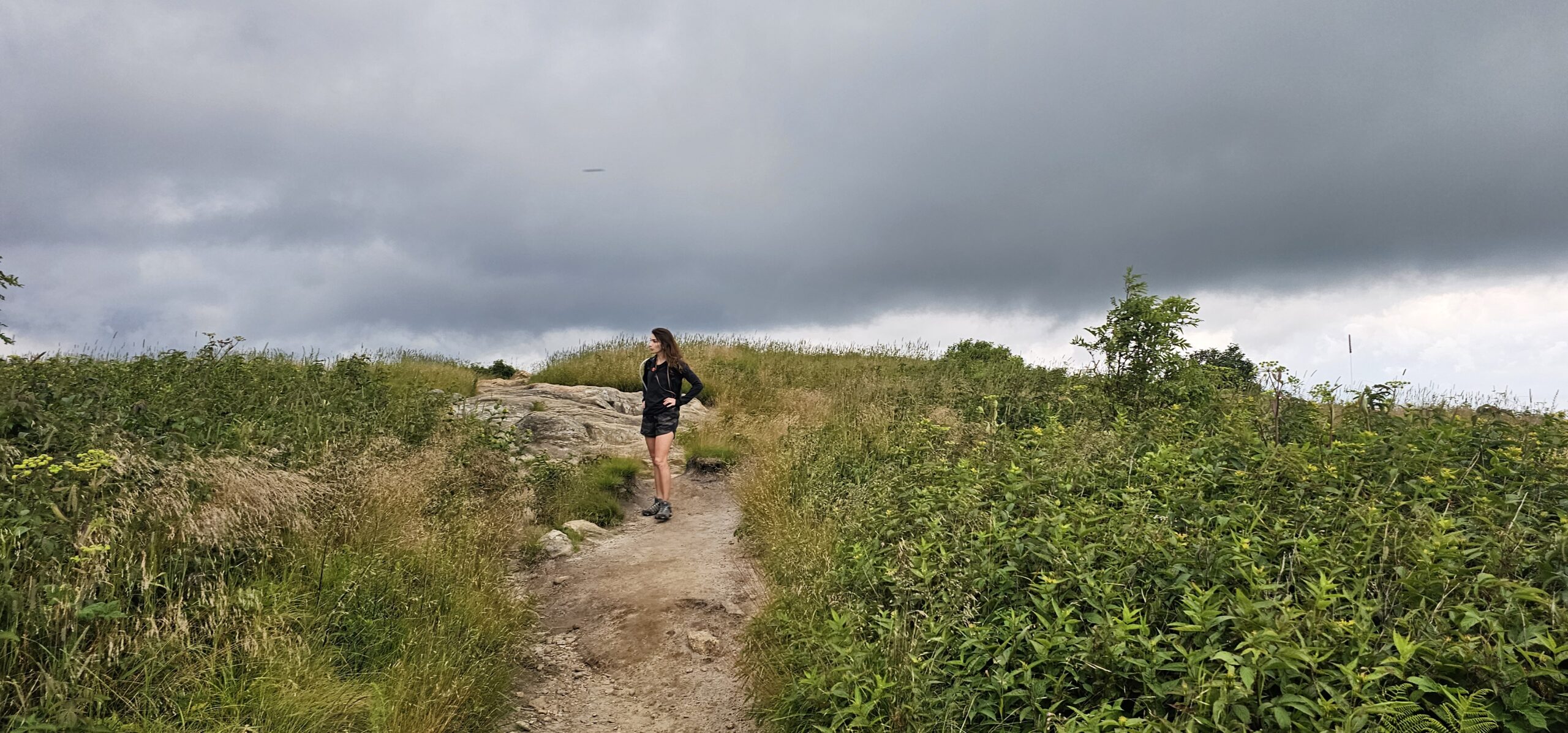 Hiker walking along grassy bald trail at Black Balsam Knob with dramatic cloud formations