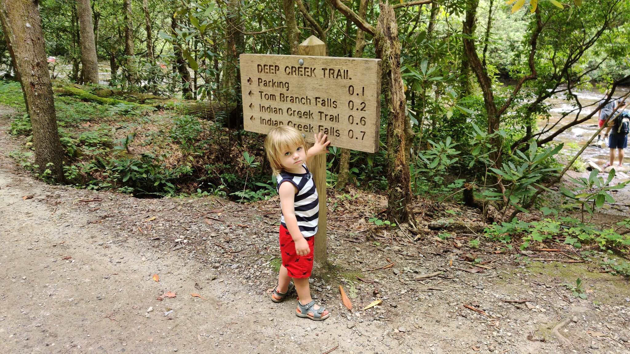 Child posing at the Deep Creek Trail sign showing distances to Tom Branch Falls and Indian Creek Falls