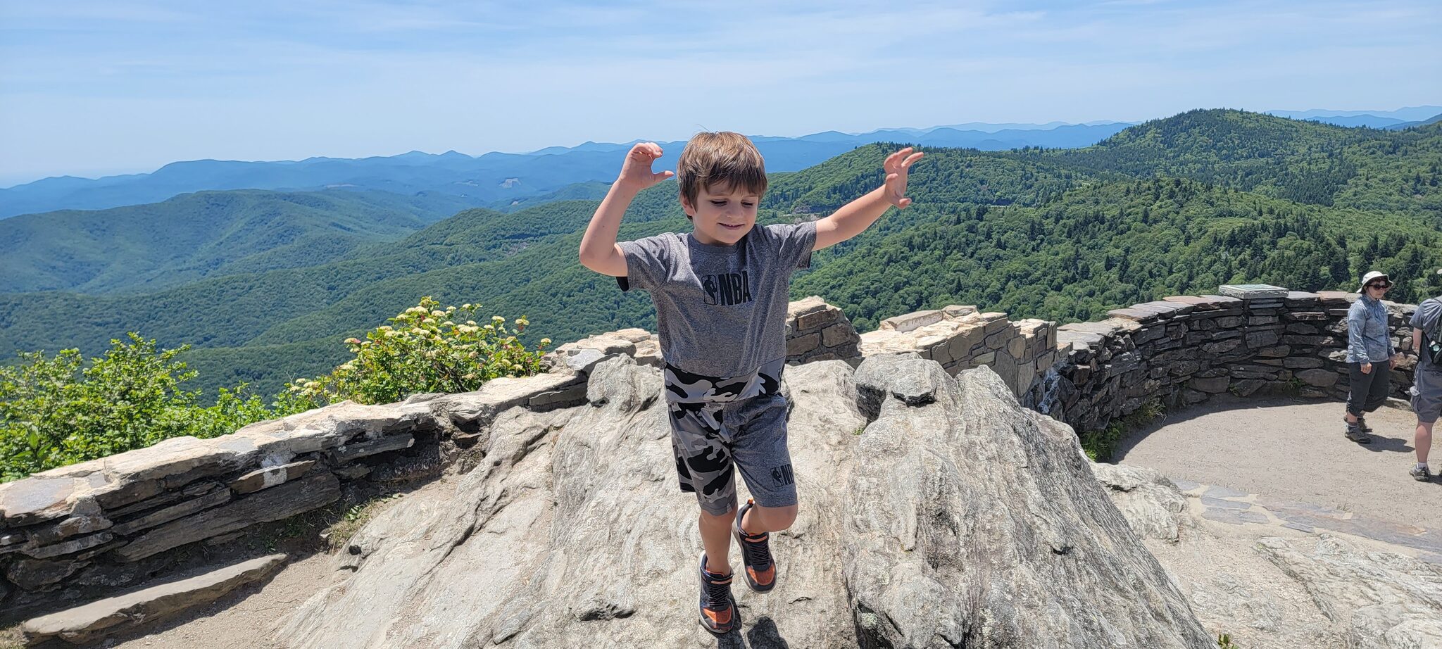 Kid jumping on the rocky summit of Devil's Courthouse with Blue Ridge Mountains in the background