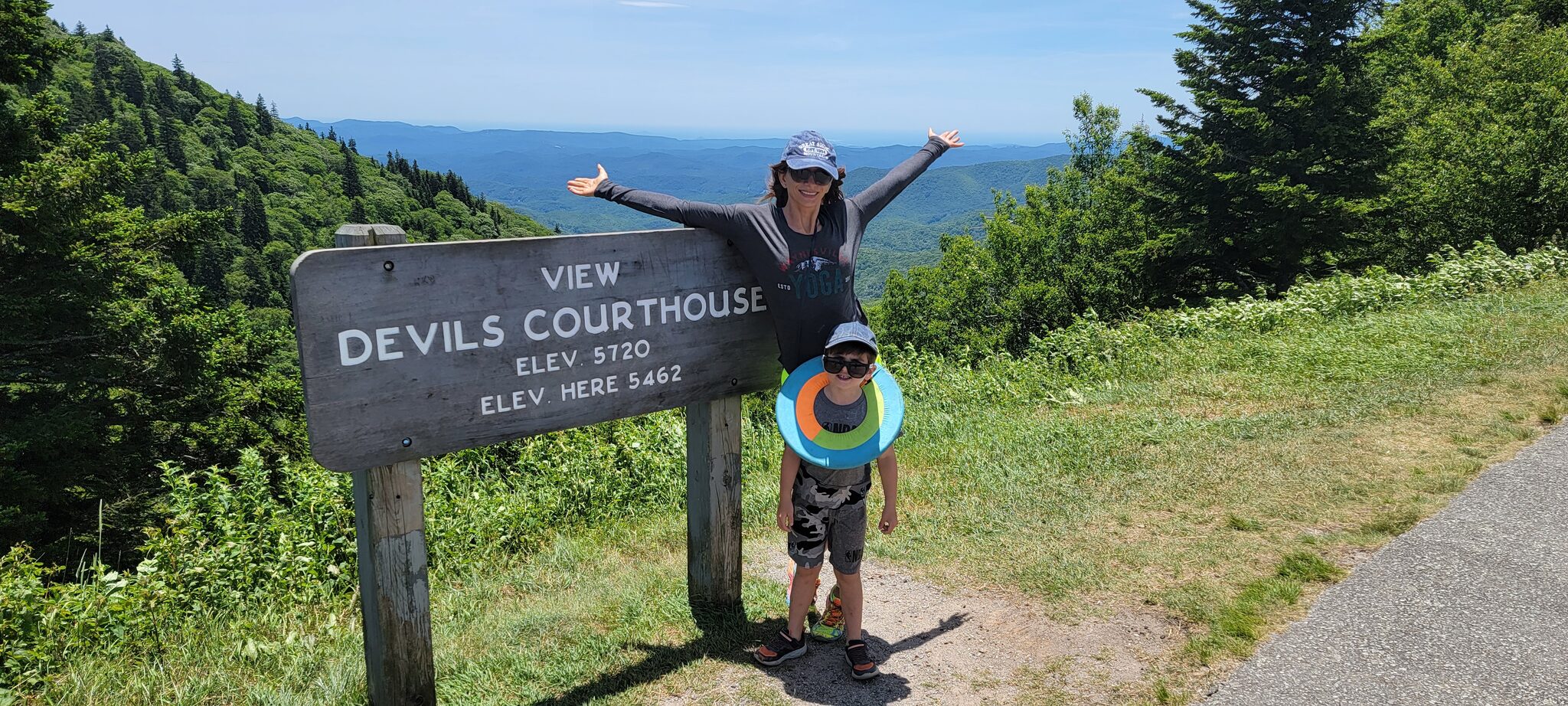 Family posing at the Devil's Courthouse trail sign on the Blue Ridge Parkway at 5720 feet elevation