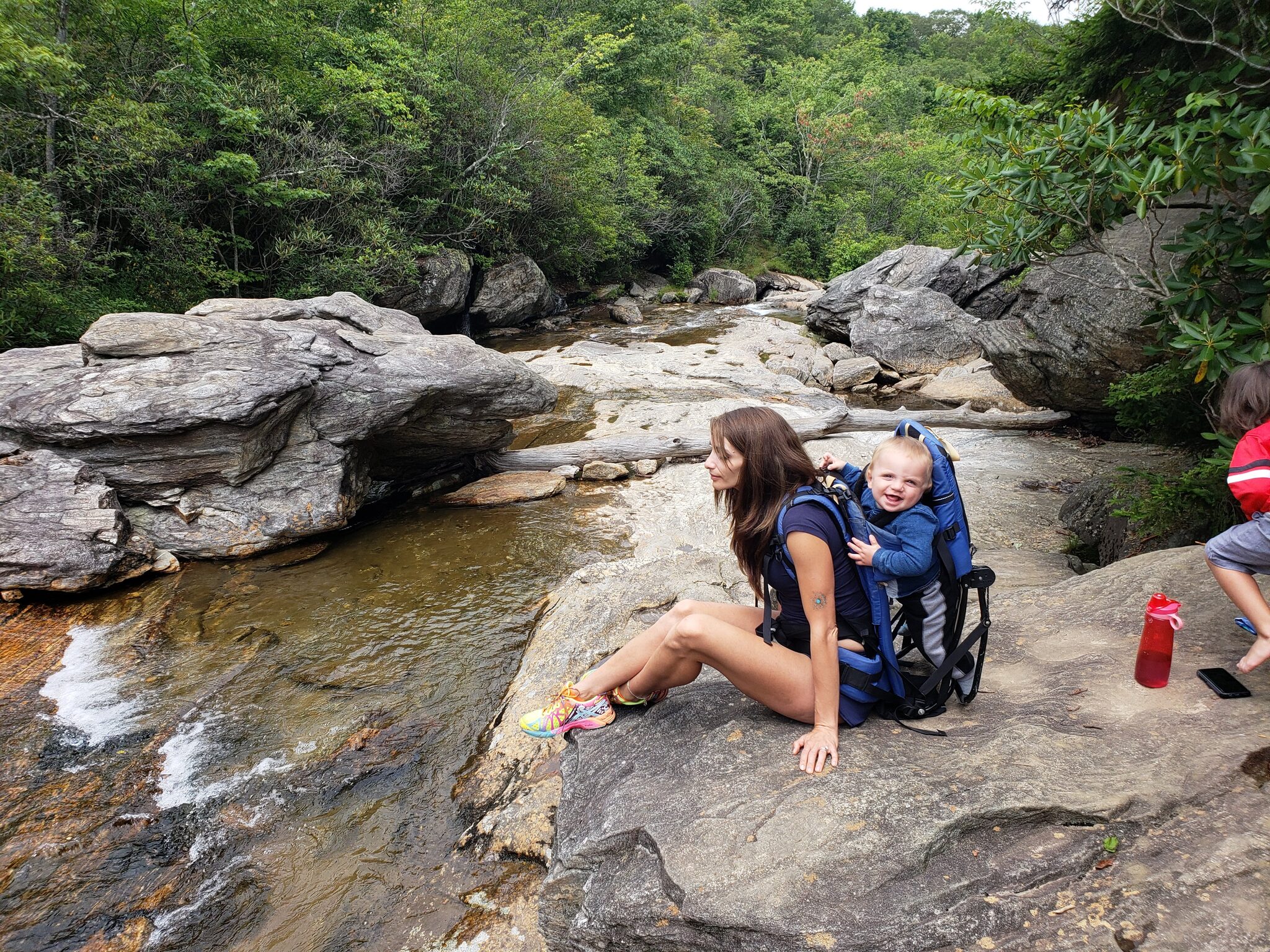 Family resting on rocks by the waterfall at Graveyard Fields with baby in backpack carrier