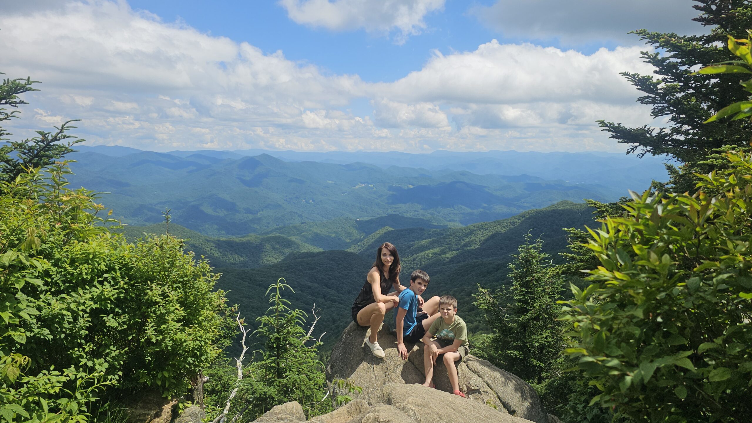Woman and child sitting on Waterrock Knob summit overlooking green mountain valleys