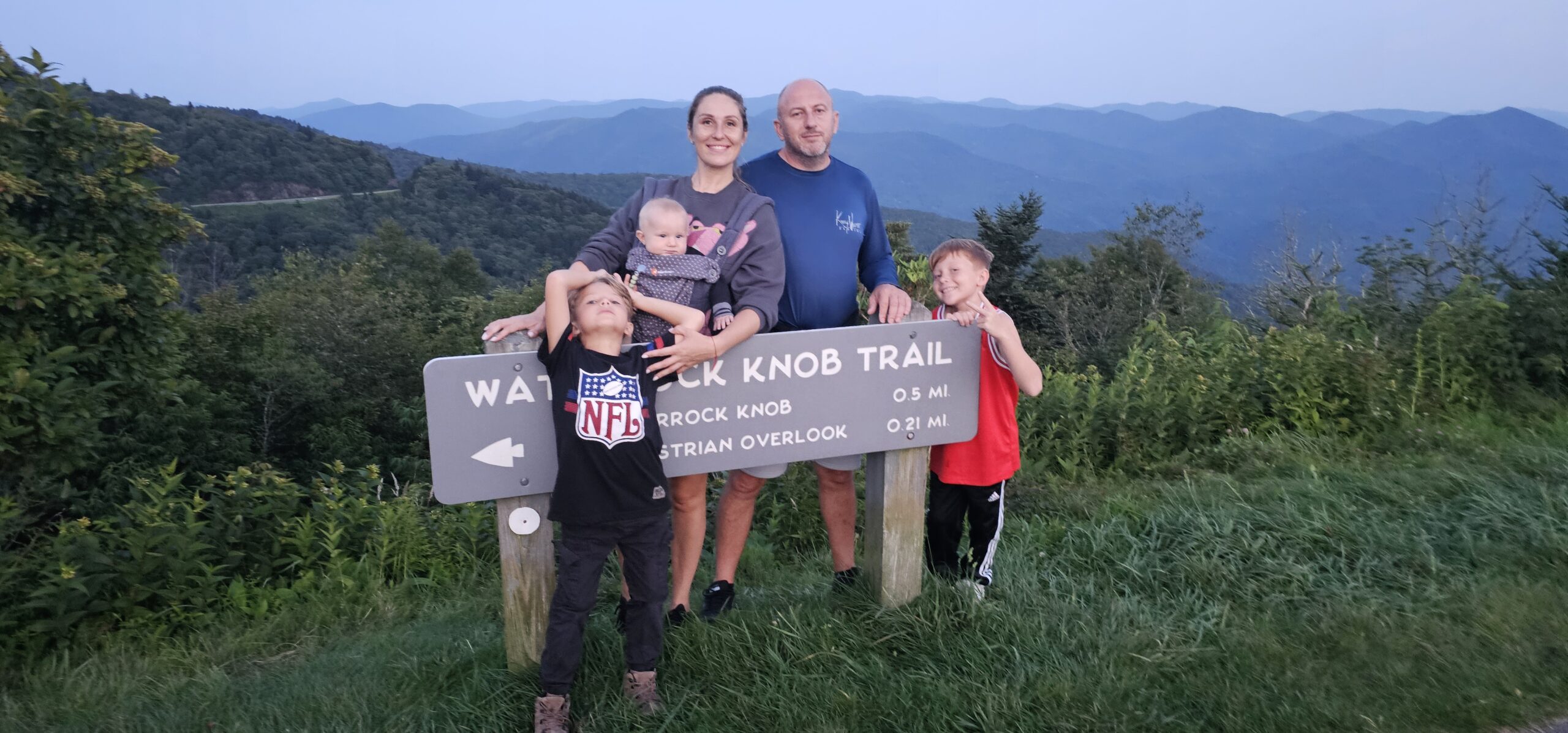 Family at the Waterrock Knob Trail sign on the Blue Ridge Parkway at dusk